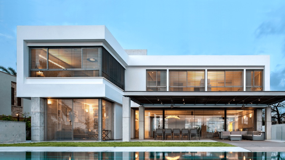 Raffstores an moderner Architekturvilla mit Pool bei Dämmerung